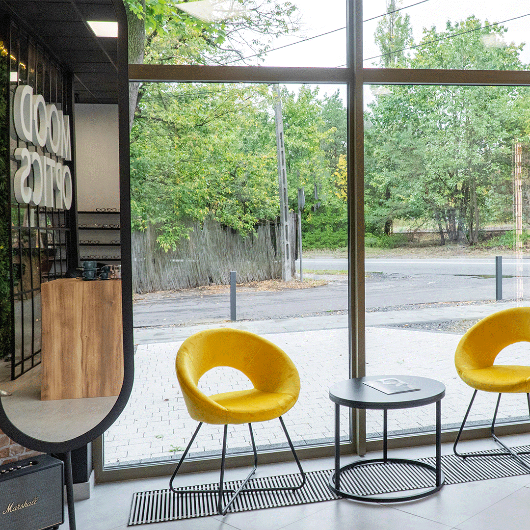 Wnętrze salonu optycznego Mood Optics. Przeszklona witryna z żółtymi designerskimi fotelami.