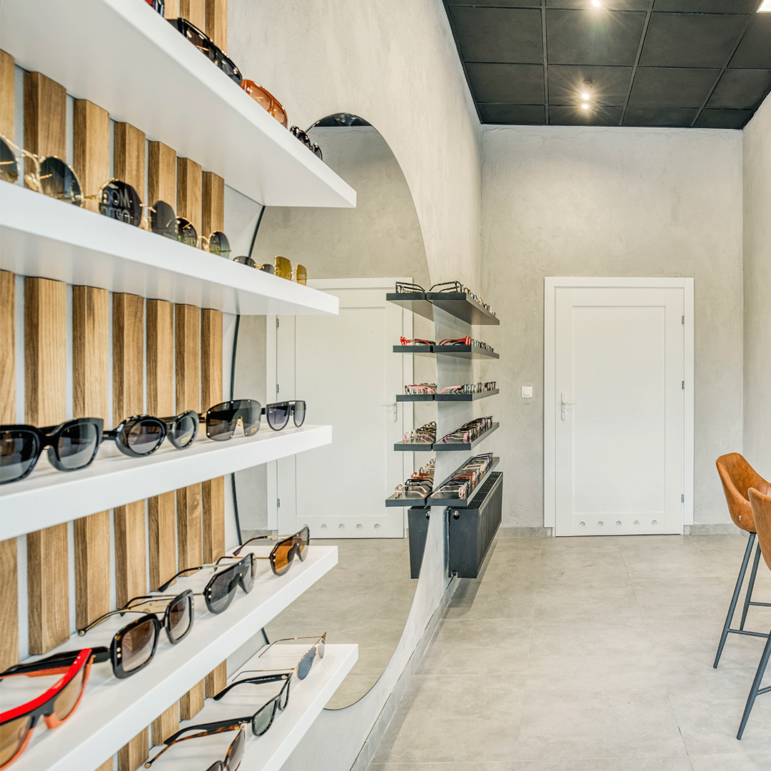 Wnętrze salonu optycznego na którym widać wyeksponowane okulary na czarno-białych półkach, po środku znajduje się okrągłe lustro.