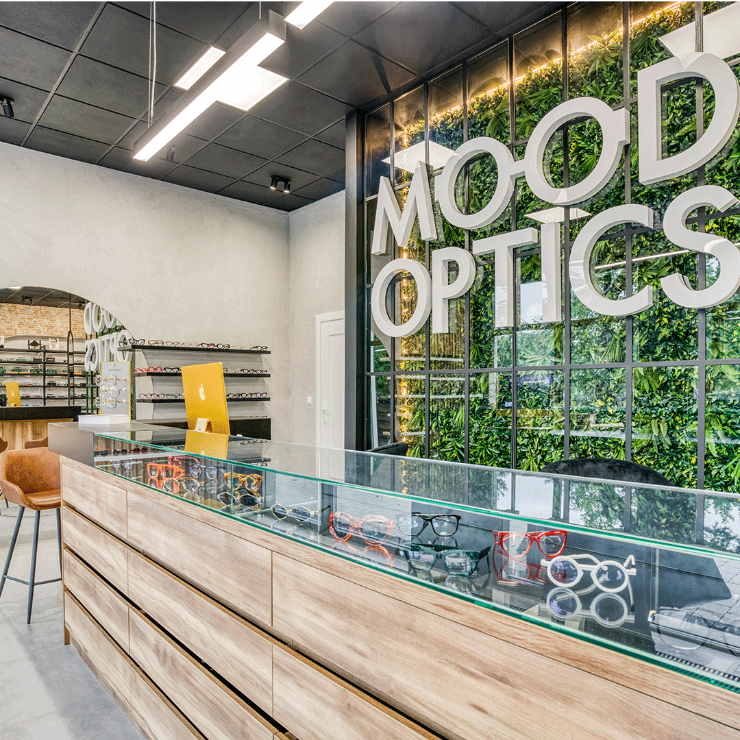Nowoczesny salon optyczny Mood Optics, wyróżniający się dużym neonem z logo oraz zieloną ścianą w stylu loftowym.