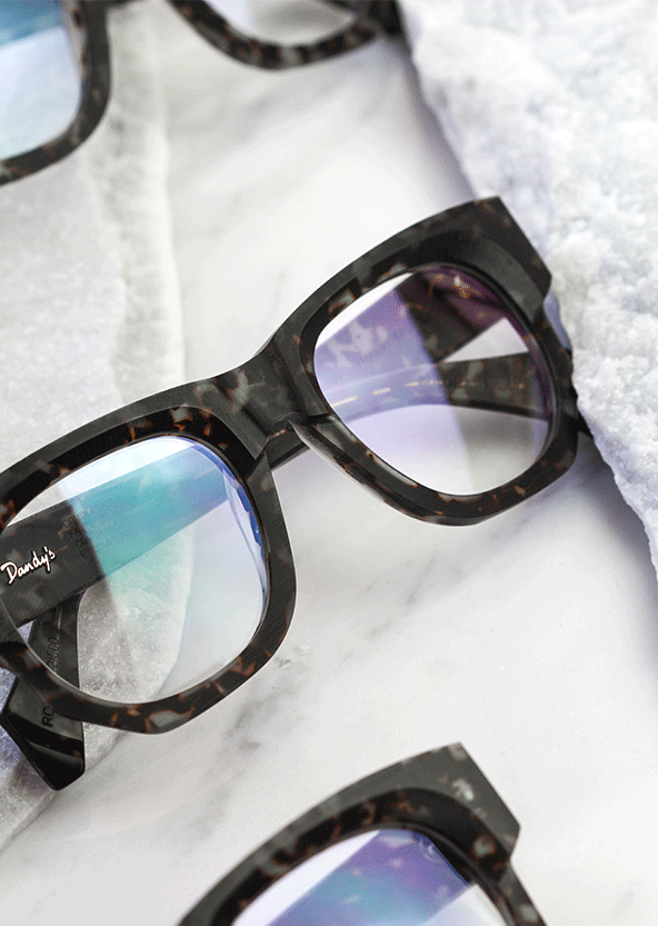 Czarne okulary korekcyjne na marmurowym blacie, tworzące elegancką kompozycję.