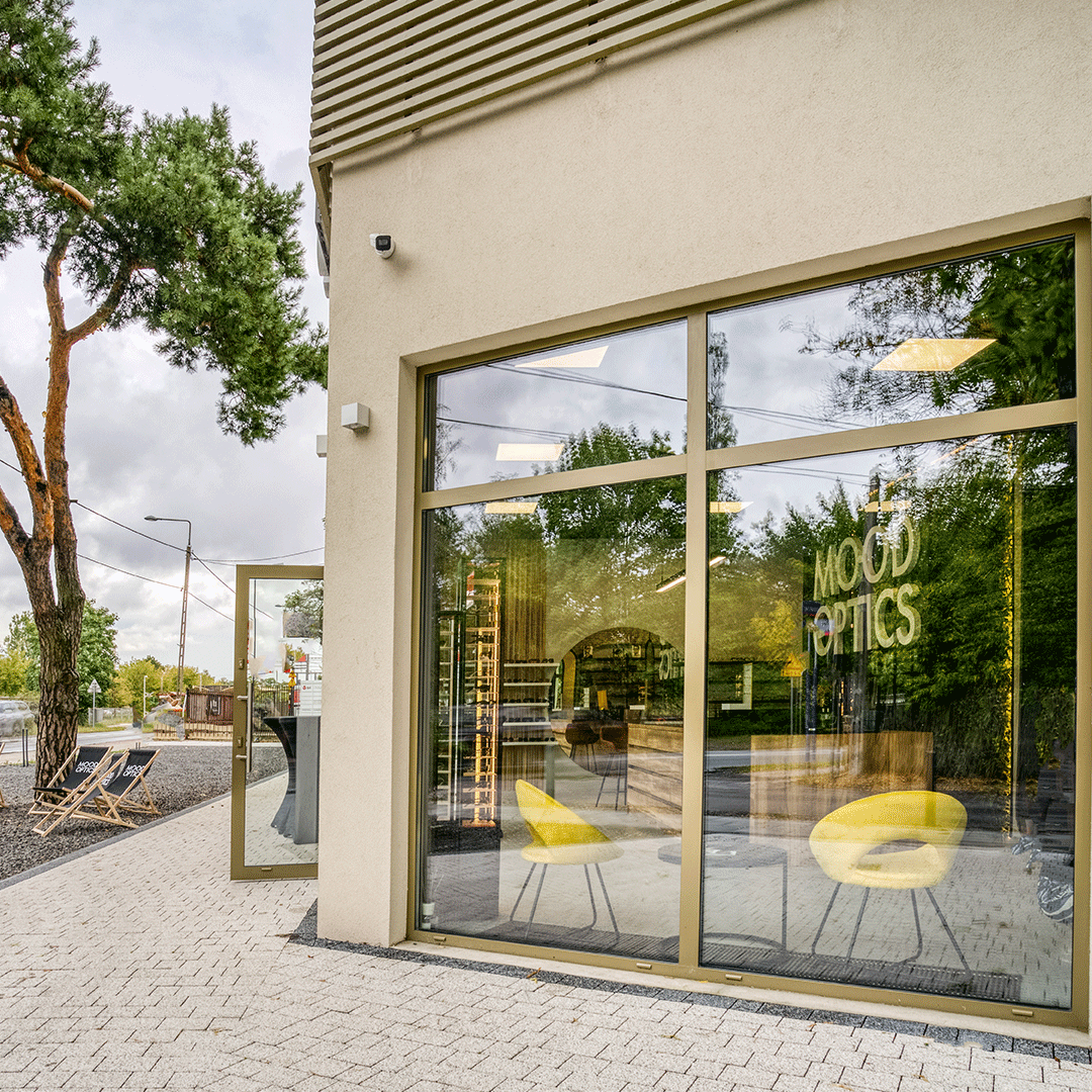 Widok z zewnątrz salonu, przez duże okna widać wnętrze salonu z żółtymi designerskimi fotelami.